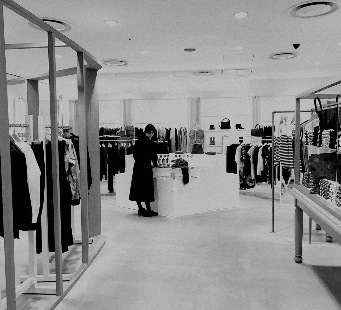 Interior de una tienda de ropa con una clienta al fondo